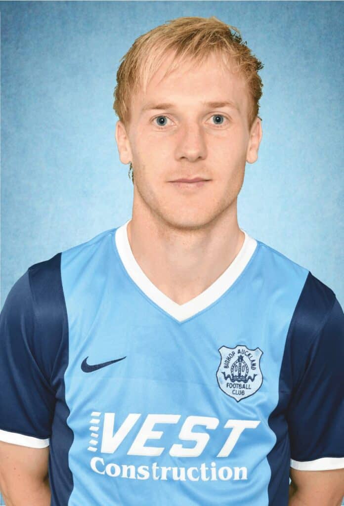 - Athlletic football player in Bishop Auckland FC kit standing against a blue background.