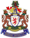 A detailed image of Bishop Auckland FC's crest featuring a crowned lion, two lions holding a shield, and the motto "Esayez" on a blue scroll, representing the club's rich heritage and identity.