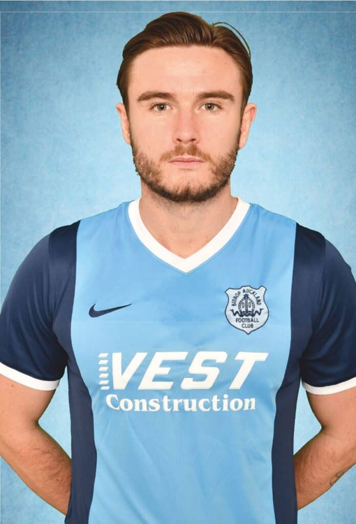 Youth football player wearing Bishop Auckland FC kit, representing local football club, sponsor VEST Construction, and sporting official team merchandise for club promotion.