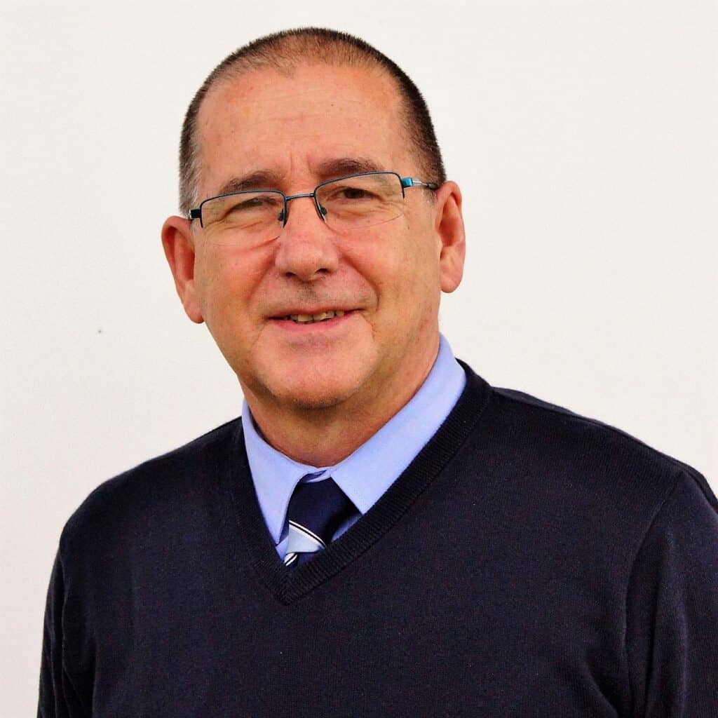 Friendly man wearing glasses smiling, dressed in smart attire, representing Bishop Auckland FC community.