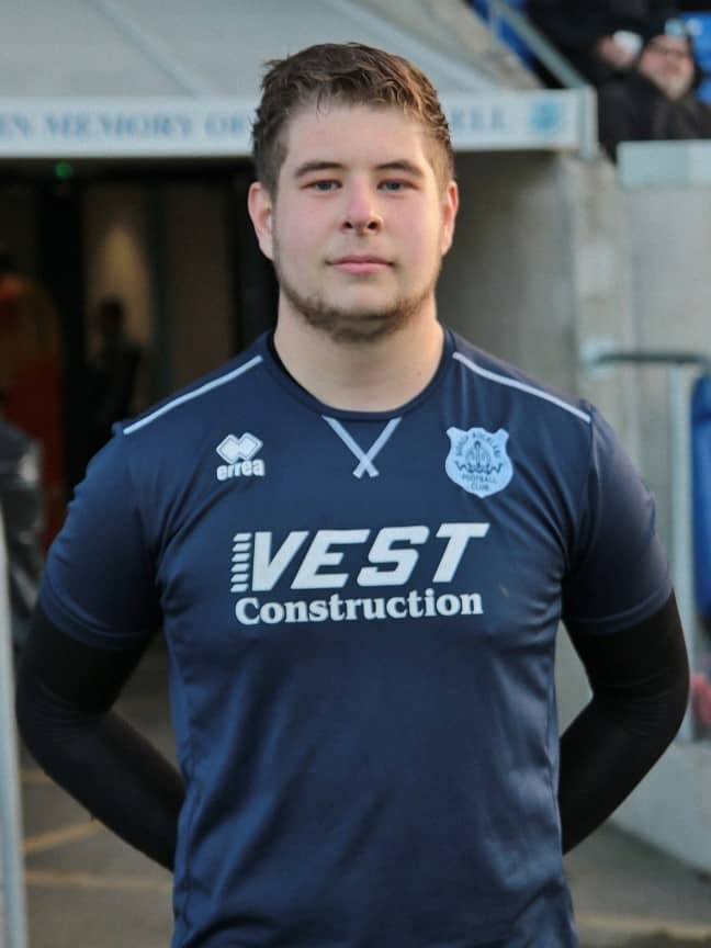 Young football player in Bishop Auckland FC kit at the stadium entrance.