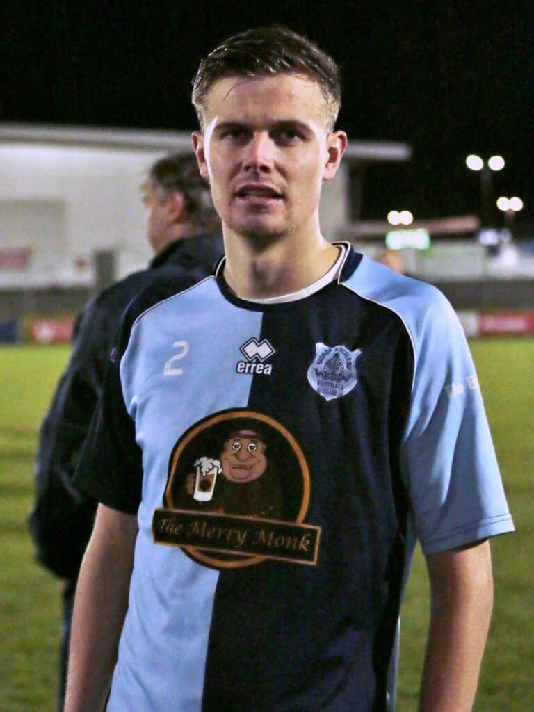 Youth football player in Bishop Auckland FC kit at night, standing on the pitch after a match, showcasing team pride and competitive spirit.