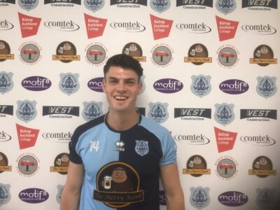 Bishop Auckland FC player in home kit posing in front of a branded backdrop at the football club.