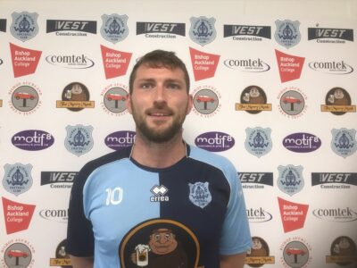Bright football player in Bishop Auckland FC kit, with club logo, standing against sponsor backdrop, showcasing team spirit, player number 10, and club pride.