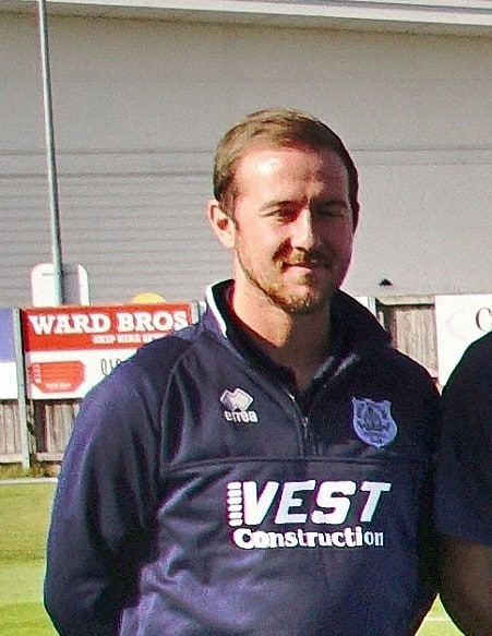 Bishop Auckland FC player in team matchday kit, celebrating a game event, showcasing club's football team spirit and community involvement.