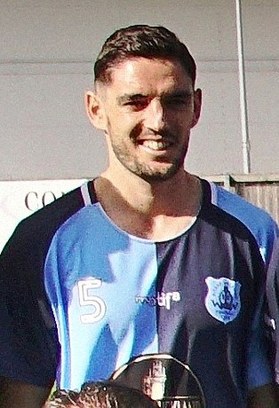 A football player in a Bishop Auckland FC kit smiling after a match, showcasing team spirit and dedication to Northern League football.