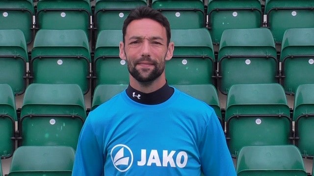 Professional Bishop Auckland FC player in team kit at the stadium.