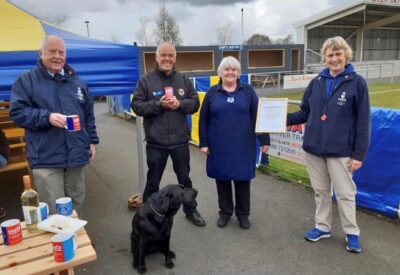 Bishop Auckland FC community event with staff and a black dog, showcasing local football club activities and community spirit in a stadium environment.