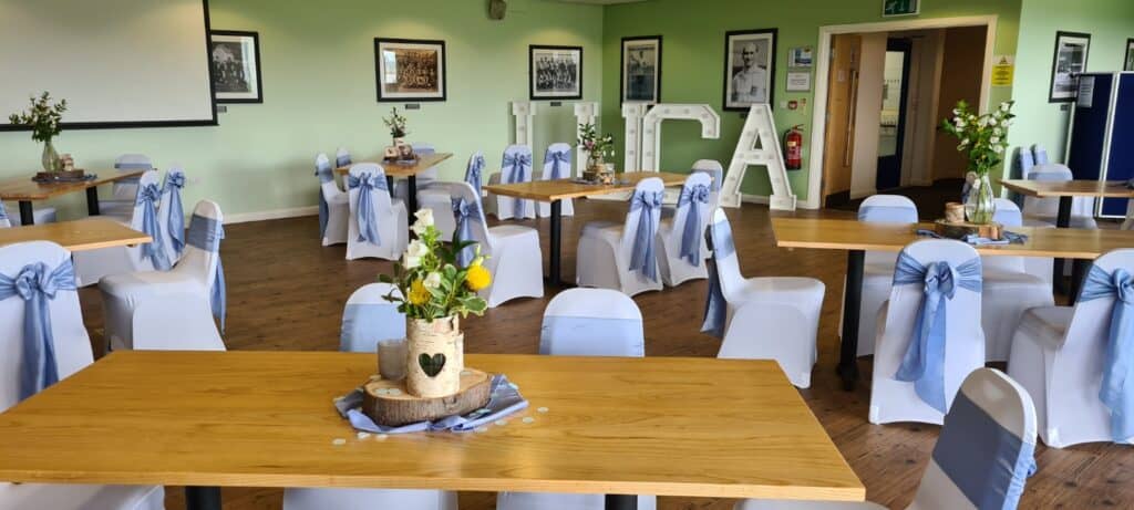 Bright, airy event space at Bishop Auckland FC with decorated tables, white chair covers with blue sashes, perfect for community gatherings and match day functions.
