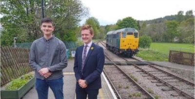 Bishop Auckland FC team members standing near train tracks with locomotive in the background, showcasing local heritage and community spirit.