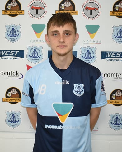 Young Bishop Auckland FC footballer in team kit, standing in front of club sponsorship banners; showcasing local football talent and club identity.