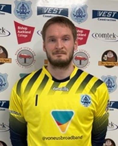 A football player from Bishop Auckland FC in team kit, standing in front of a branded backdrop, showcasing the team’s player roster and organisation.