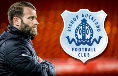 Experienced football coach watching Bishop Auckland FC match with club logo in background.