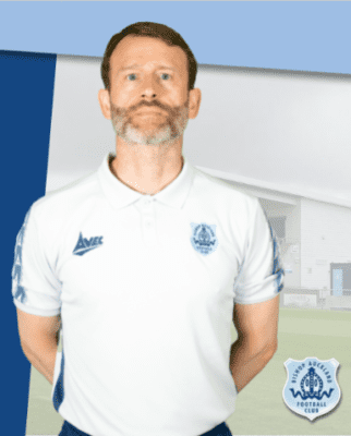 Experienced Bishop Auckland FC coach standing on the football pitch, promoting local football excellence and community engagement.