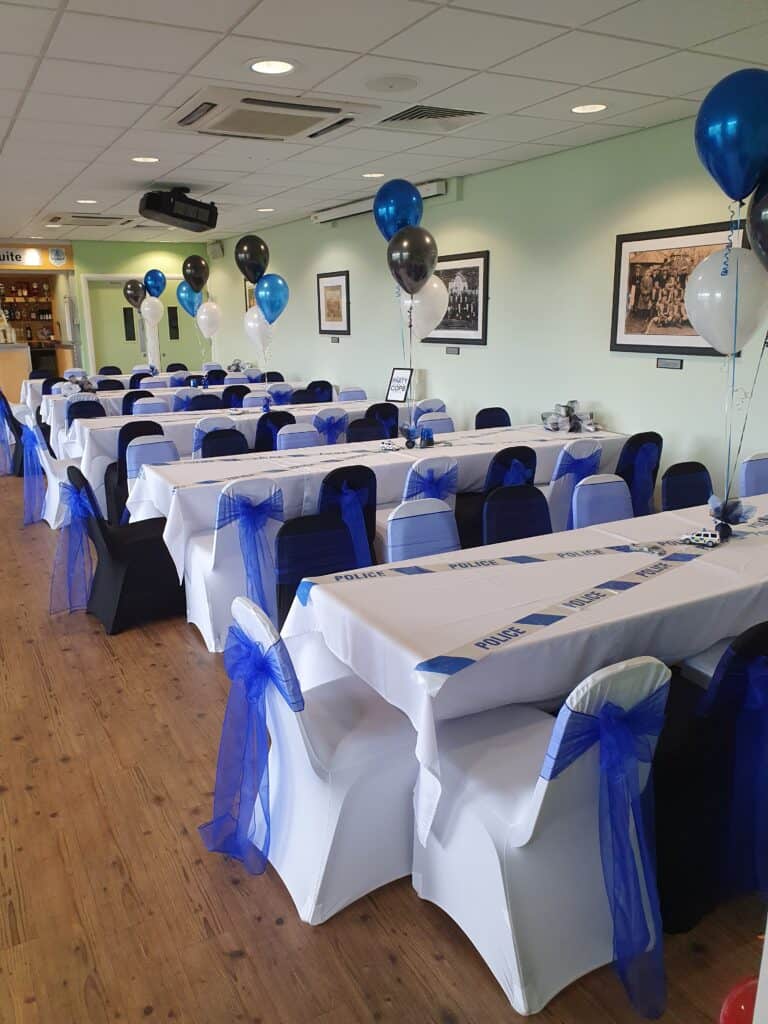 Colour-themed table decorations with police tape and balloons, suitable for a police-themed event hosted by Bishop Auckland FC at a community venue.