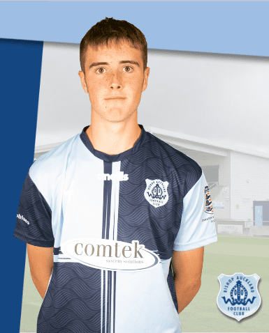 A young male football player in Bishop Auckland FC kit standing indoors against club background.