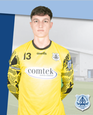 Teenage goalkeeper in yellow kit with Bishop Auckland FC badge, standing in front of football stadium, promoting local football club and youth sports development in County Durham.