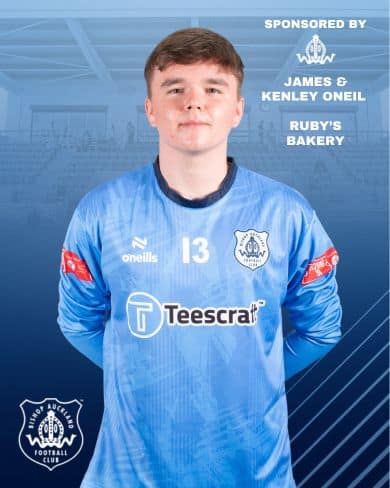 Young football player in blue Bishop Auckland FC kit standing on the pitch, showcasing team pride and player readiness for upcoming matches.