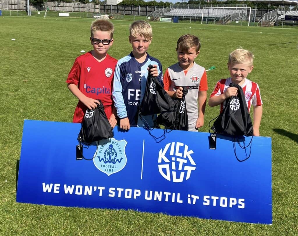 Young boys in football kits holding goodie bags on a football pitch, celebrating youth football development at Bishop Auckland FC.