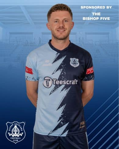 A young male football player wearing Bishop Auckland FC kit, smiling confidently against a blue background.